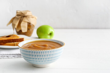 Bowl with sweet apple jam and toasts on light wooden background