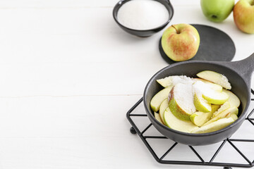 Frying pan with cut apples and sugar on light background