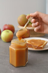 Female hand with spoon and jar of tasty apple jam on dark table