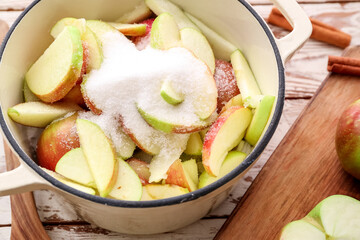 Cooking pot with cut apples and sugar on wooden background