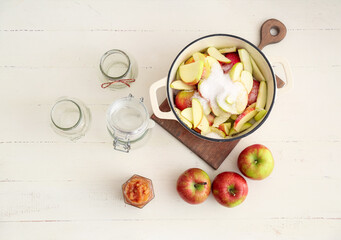 Jar with jam, cooking pot with cut apples and sugar on light background