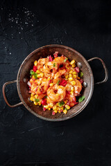 Spicy shrimps with maize in a pan, shot from above on a black background