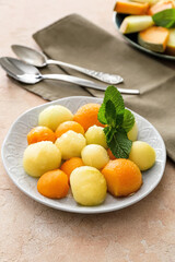 Plate with sweet melon balls on color background