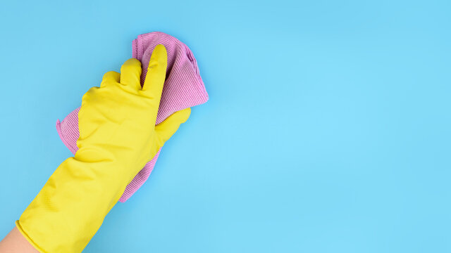 Hand in yellow glove with rag on blue background cleaning concept with free space for text