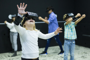 Emotional happy preteen girl in vr headset goggles playing exciting virtual reality game, touching...