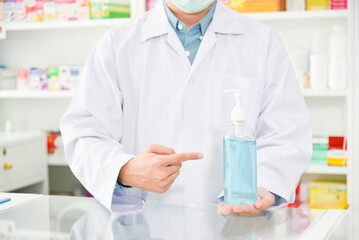 Pharmacist holding alcohol gel bottle and pointing to it at drugstore.