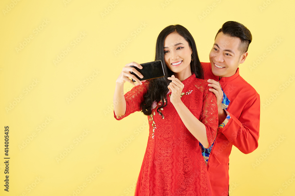 Sticker Smiling Vietnamese boyfriend and girlfriend talking selfie in traditional dresses, isolated on yellow