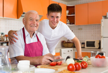 Obraz na płótnie Canvas Cheerful senior man and his grandson cooking together in kitchen