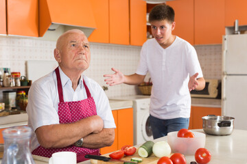 Teenage boy lecturing his senior grandfather sitting at table in kitchen