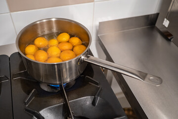 Preparation of mandarins in syrup. On the stove is a ladle of tangerines and syrup. Whole tangerines in the peel are cooked in syrup. Meals of the citrus. The dessert of citrus.