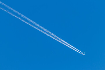 Flying airplane on a journey through the blue sky with a long white smoking exhaust plume and jetwash shows international transportation and globalization transatlantic holidays with pilots
