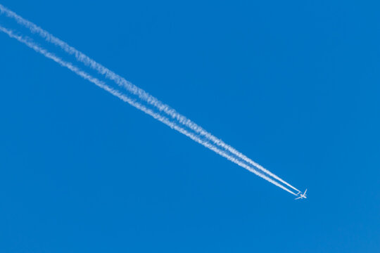 Flying airplane on a journey through the blue sky with a long white smoking exhaust plume and jetwash shows international transportation and globalization transatlantic holidays with pilots