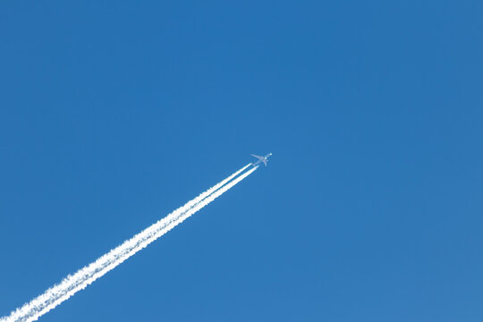 Flying airplane on a journey through the blue sky with a long white smoking exhaust plume and jetwash shows international transportation and globalization transatlantic holidays with pilots