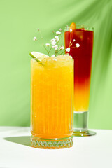 Mango lemonade drink over green background. White table with sunlight and palm leaf hard shadow. Summer, tropical and juicy concept