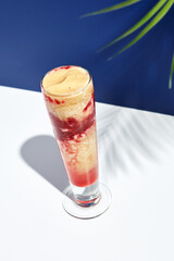 Raspberry and banana smoothie over white and blue background. Palm leaf with sunshine and hard shadow. Fruit yogurt or shake drink in high glass. Summer, healthy, fresh drink concept