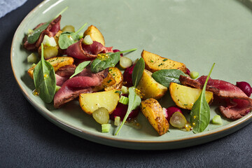Salad with roast beef and baked potato. Garnished with fresh spinach. Green dish on Black textured table. Restaurant, gourmet food concept