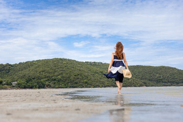 Woman barefoot hold hat and walking on summer along wave of sea water and sand on the beach.