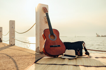 Hat, Bag and Guitar on reed mat near the sea at sunset. Travel, vocation, holiday, summer concept.