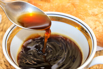 A mug of black coffee, where a hot drink is cooled with a spoon.