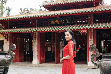 Beautiful young Asian woman in red lace dress standing at Buddhist temple and smiling at camera
