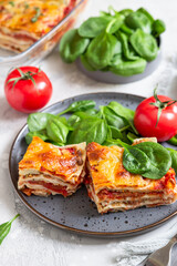 Italian lasagna with tomato sauce and cheese served with tomatoes and spinach, light concrete background. Homemade vegetarian lasagna.