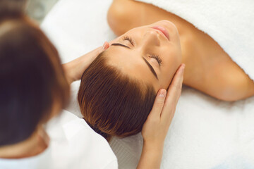 Fototapeta na wymiar Close up hands of young woman masseur doing facial massage to beautiful woman at spa salon.
