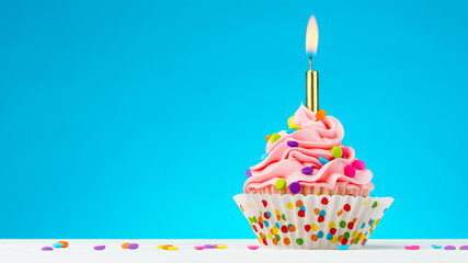 Birthday cupcake. Tasty cupcakes with pink cream icing and colored sprinkles. Burning candle in a cupcake. Sweet delicious dessert on natural white wooden table and blue background. Happy Birthday. 