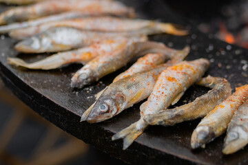 Process of cooking european smelt fish with red paprika powder on black brazier at summer outdoor food market: close up. Seafood, barbecue, gastronomy, cookery, street food concept
