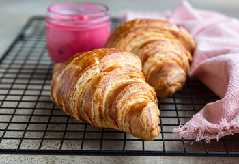 Fresh crispy croissants with pink honey on black metal grille, concrete background.