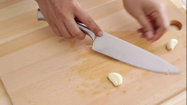 young wife chopping garlic in top of square chopping wooden board at kitchen table