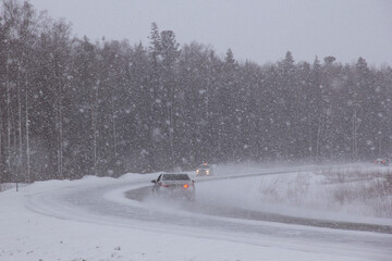 A road covered by a blizzard. Cars drive along the highway in the North in heavy snow.