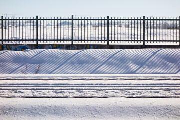 Snowy train tracks in Coslada with a fence and its shade in the background, on a cold winter's day.