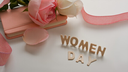 Women's Day message with notebook, pink roses and ribbon decorated on white background