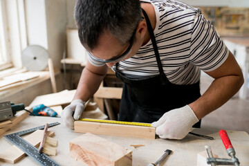 Man carpenter measuring a wooden board with a ruler with scale in workshop. Joinery work on the...
