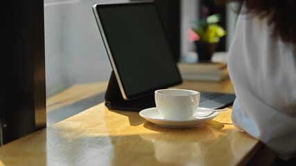Coffee cup and digital table on wooden bar with female customer in cafe