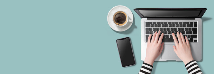 カラフルなテーブルの上で、ノートパソコンにタイピングしている女性の手。スマートフォン、コーヒー。