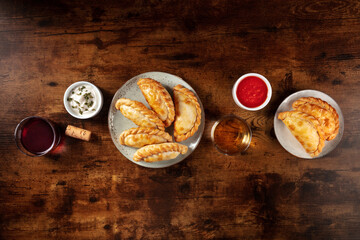 Empanadas, shot from the top with wine and sauces, with a place for text, on a dark rustic wooden background