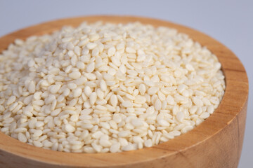 A close up of white sesame seeds in a wooden cup isolated on a white background.