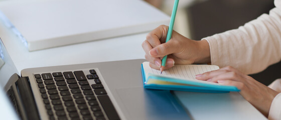 Female hand writing on notebook while working with laptop on the table