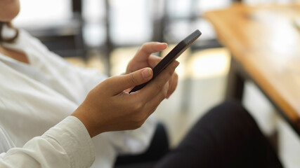 Female hands holding smartphone while sitting in workplace