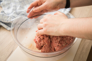 Hand von Frau mischt Hackfleisch halb und halb roh von Rind und Schwein mit Gewürzen in Schüssel...