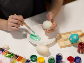 Female hand painting easter eggs, preparing for easter festival with poster colour and tools