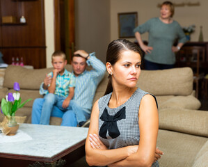 Upset young woman sitting at sofa during quarrelling between family on background at home