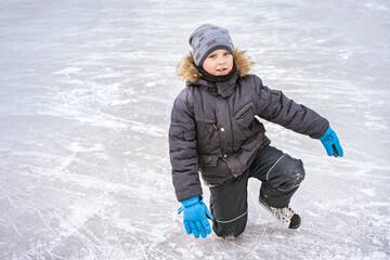 cute caucasian preschooler boy learn to skate on ice rink. Kid wearing winter jacket standing on...