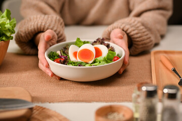 Female hands holding a plate of of salad with boiled eggs, lettuce and tomato