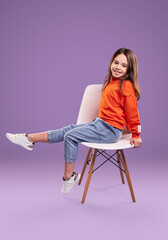 Happy little girl in casual outfit sitting on chair
