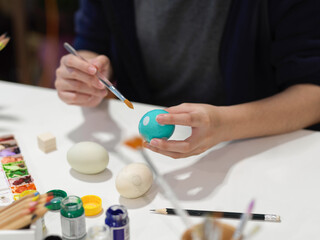 Female hands painting Easter eggs with poster colour and other paint tools