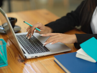 Female holding pencil in her hand and typing on laptop keyboard on workspace