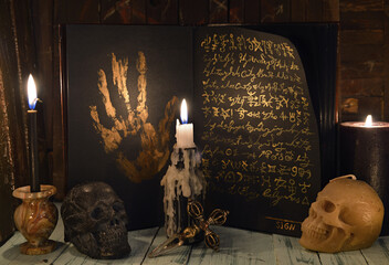 Sell soul to the devil concept with open book full of golden mystic symbols, skull and candles.