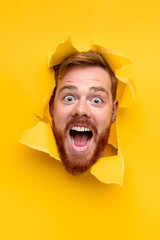 Excited man screaming through hole in paper - obrazy, fototapety, plakaty